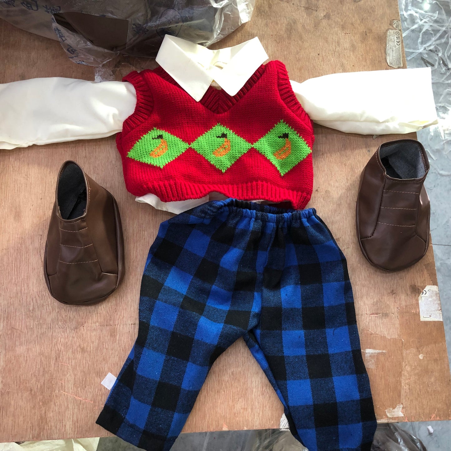 Red sweater with green accents and blue plaid pants on a cardboard surface with brown shoes.